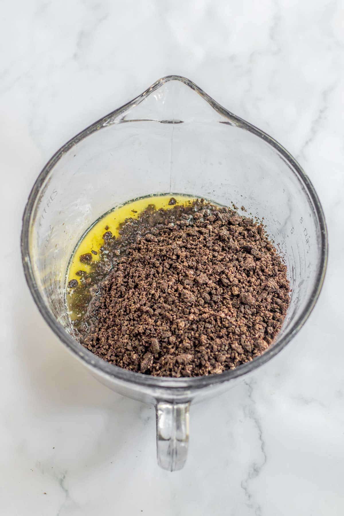 A glass mixing bowl filled with oreo cookie crumbs over melted butter.
