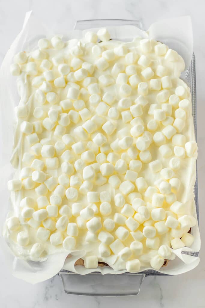 A baking dish with mini marshmallows and whipped cream.