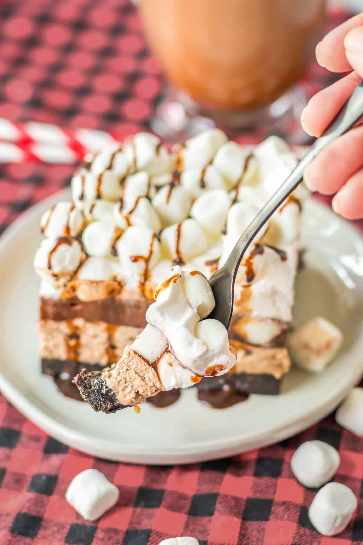 A person holding a fork with a bite of chocolate oreo delight dessert with mini marshmallows.