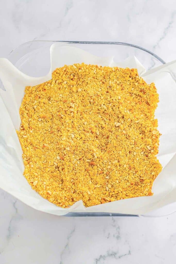 A glass baking dish with the bottom layered with buttered wafer pretzel mix.