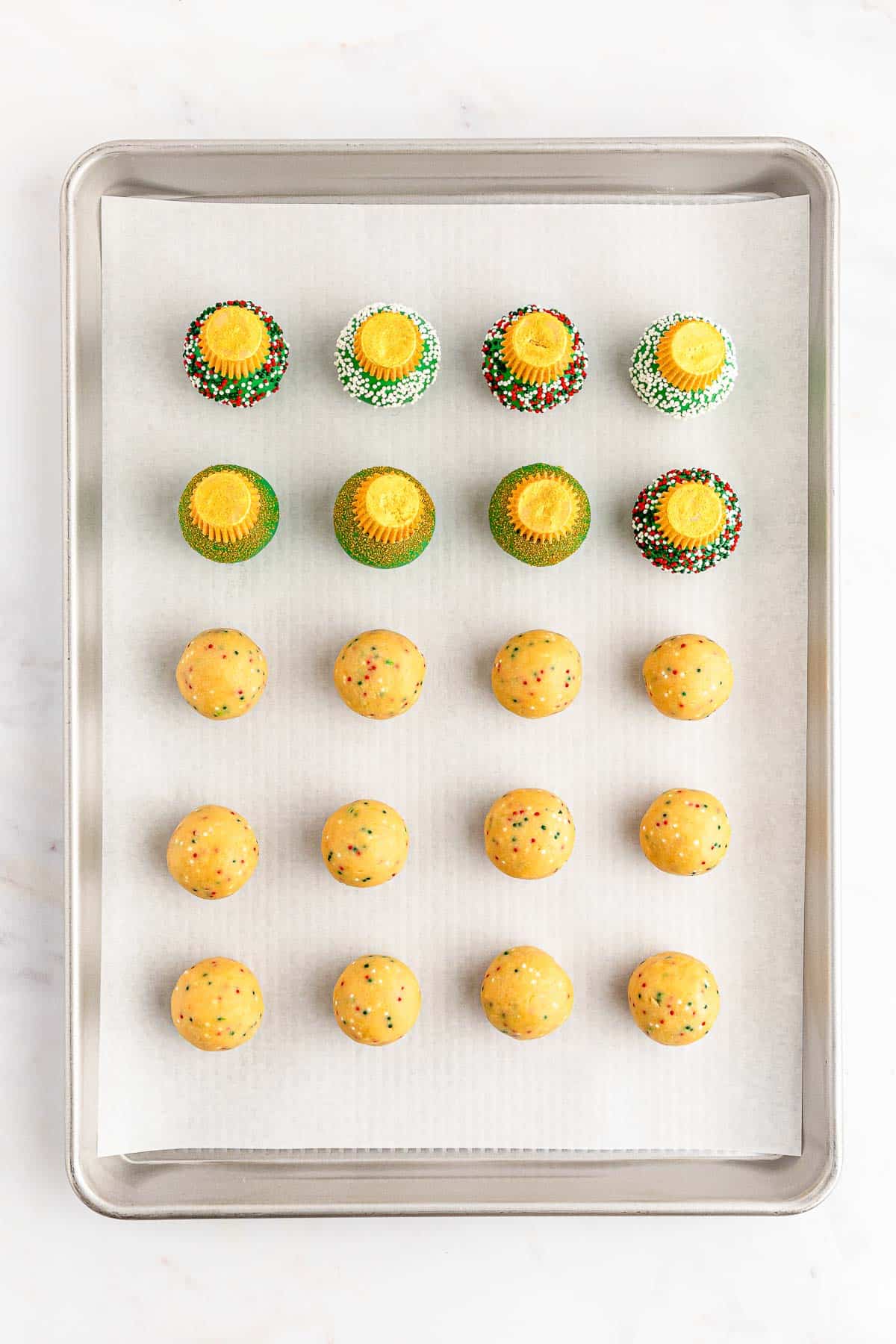 A baking sheet with golden oreo balls with some dipped in green candy. cupcakes on it.