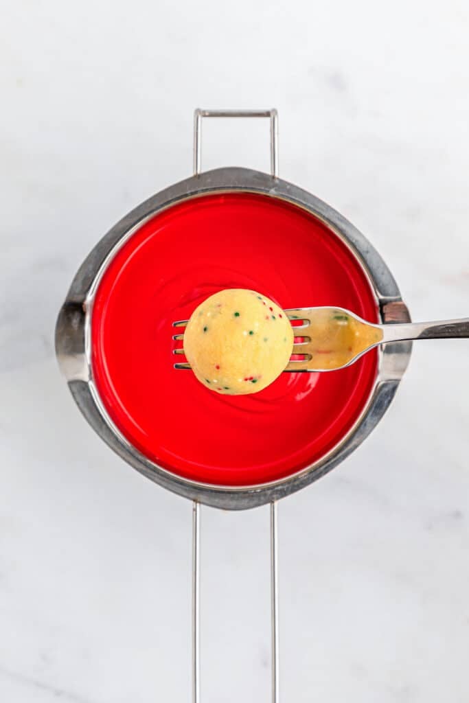 A fork holding golden Oreo ball over red melted candy.