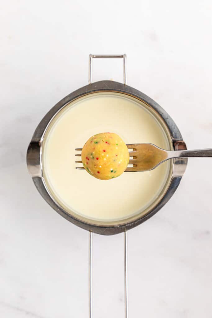 A fork holding golden Oreo ball over white melted candy.