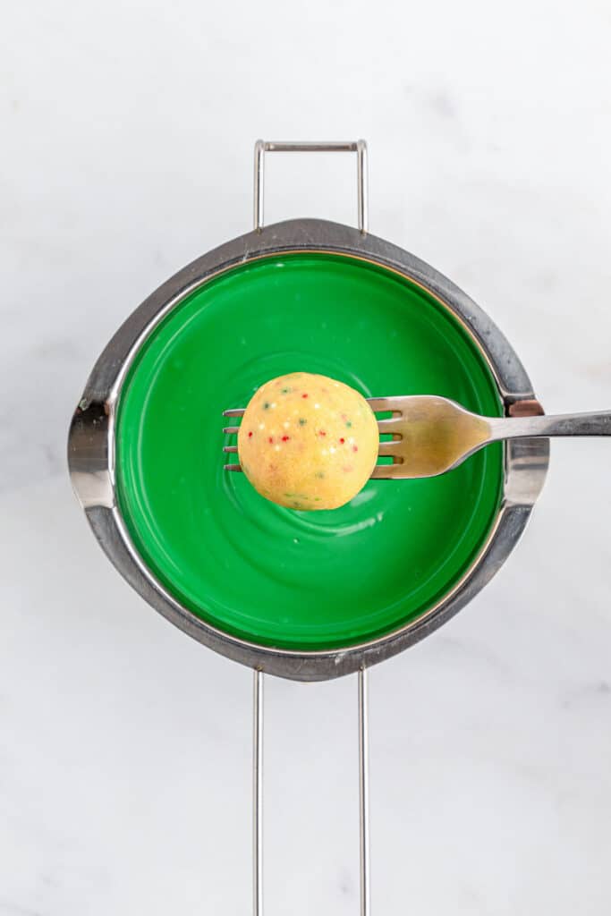 A fork holding golden Oreo ball over green melted candy.