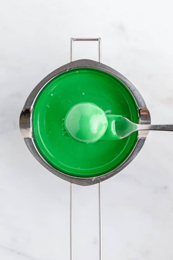A fork holding a green dipped ball over a pot of green melted candy wafers.