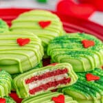 A red plate of Grinch oreos with green frosting and candy hearts on it.