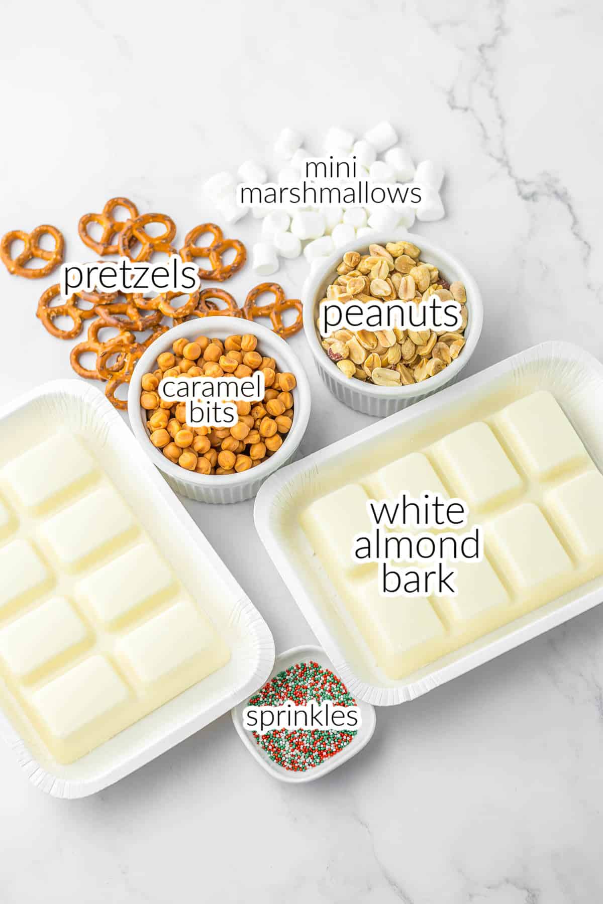 Ingredients for crockpot candy - mini marshmallows, white almond bark, caramel bits, sprinkles, pretzels and peanuts.