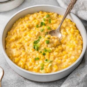 Crockpot creamed corn in a white bowl with a spoon inserted.