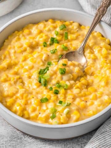 Crockpot creamed corn in a white bowl with a spoon inserted.