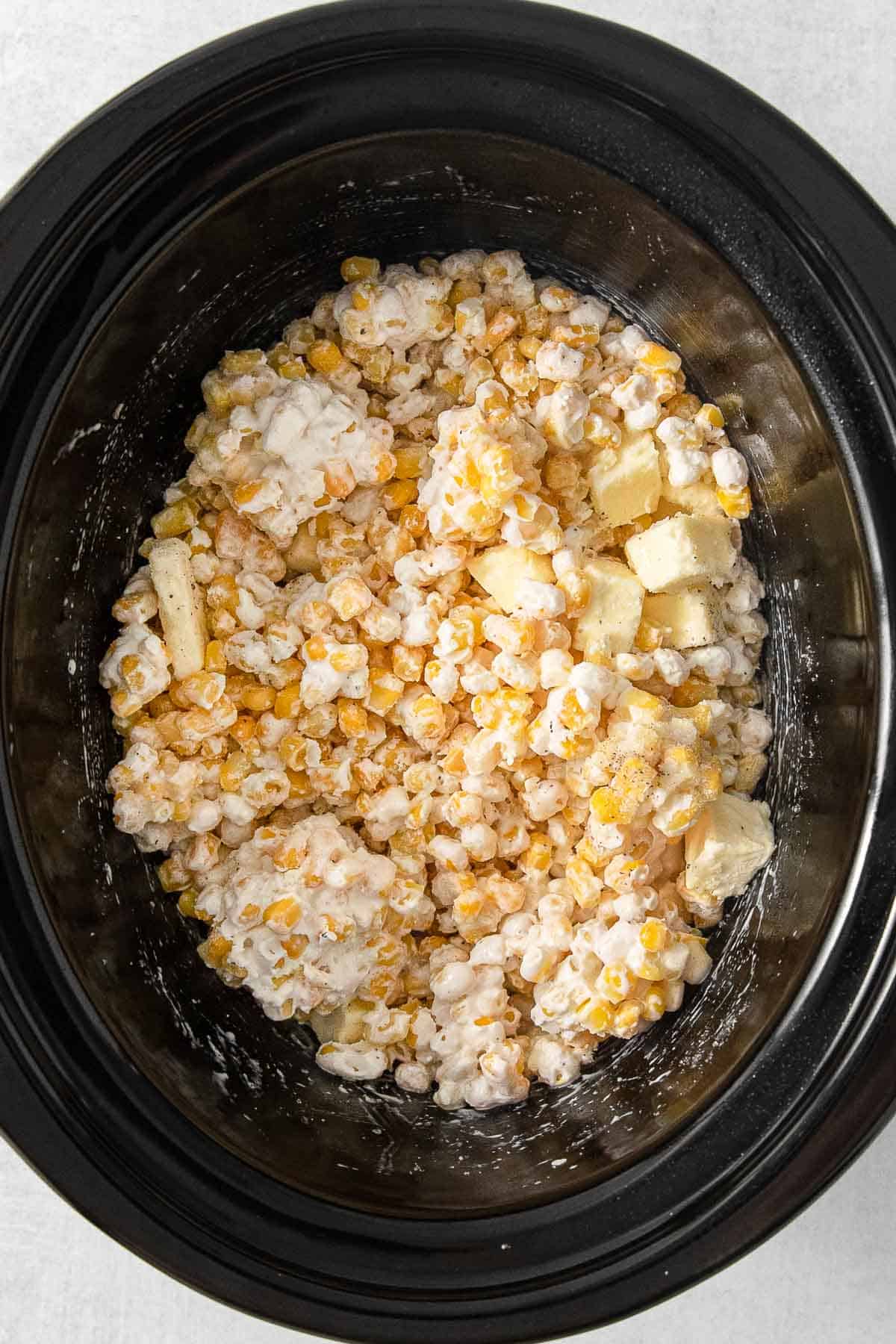 A crockpot with butter, salt, pepper and corn mixed together.