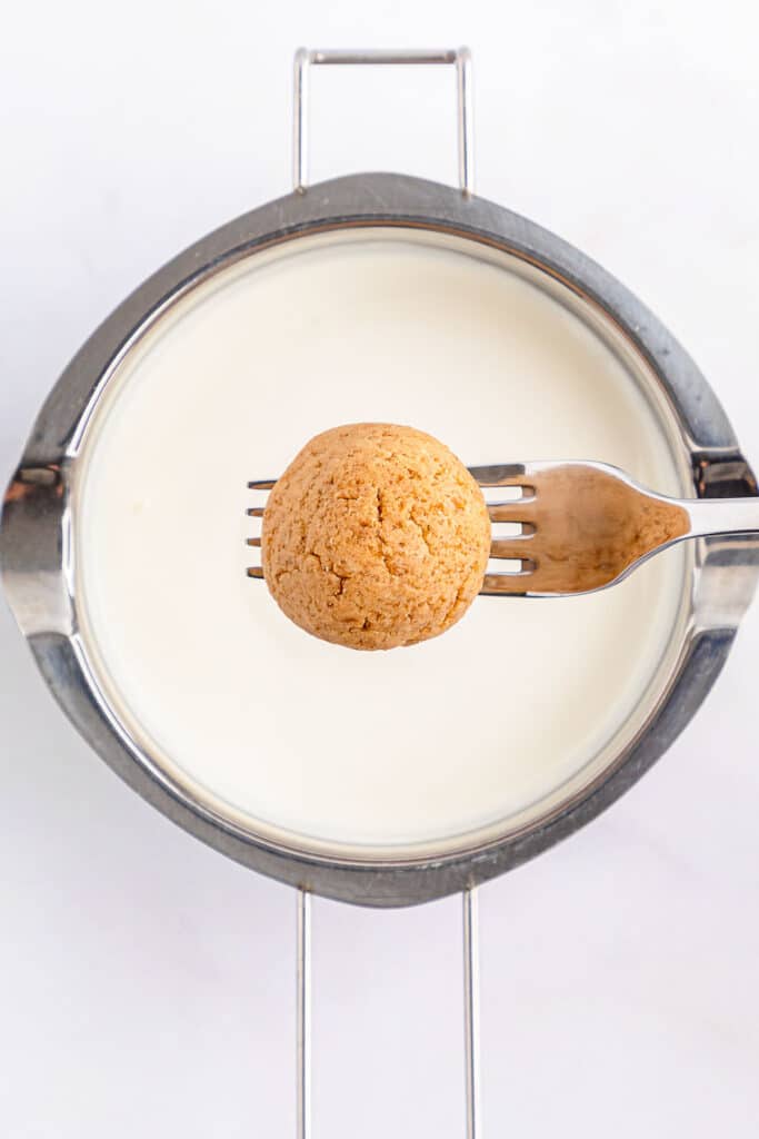 A fork with a dough ball on it hovering over the vanilla candy melt.