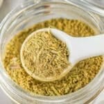 A white teaspoon full of homemade poultry seasoning over a glass jar.