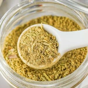 A white teaspoon full of homemade poultry seasoning over a glass jar.