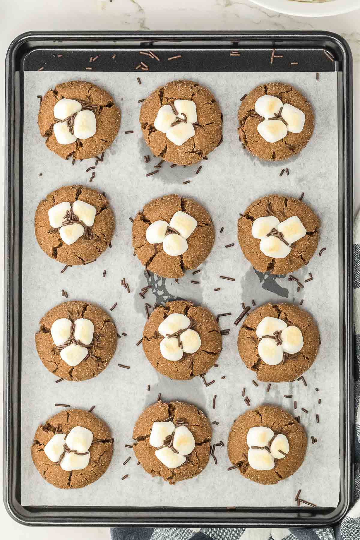 Hot chocolate cookies on a baking sheet topped with mini marshmallows.