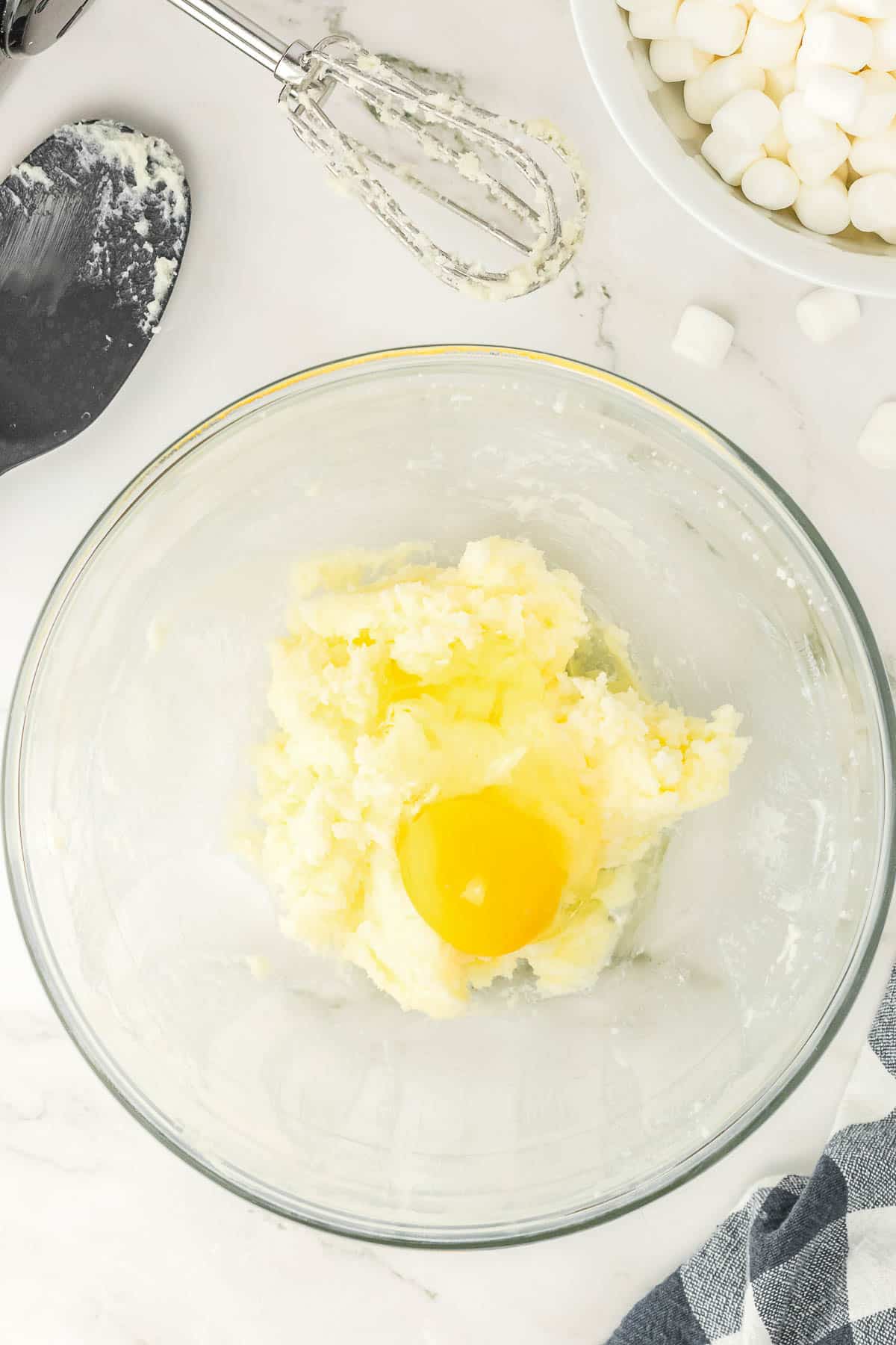 Egg added into glass bowl of butter and sugar mixture.