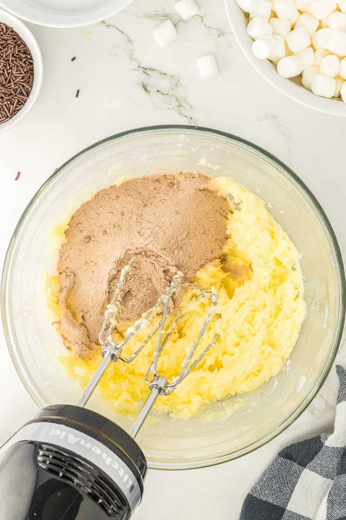 A glass bowl with the butter and chocolate mixture being mixed together with a hand mixer.