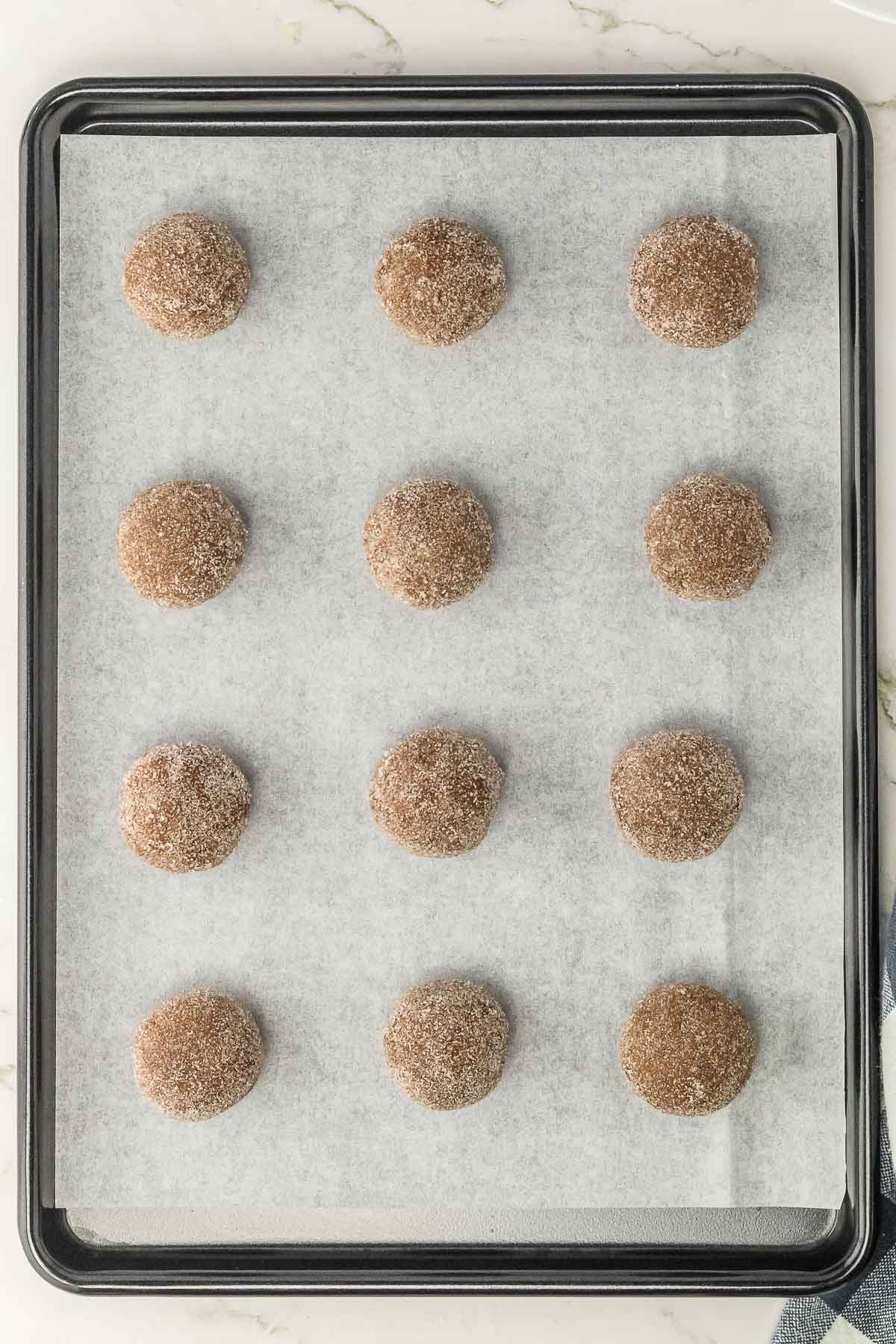 A baking sheet filled with dough balls covered in cinnamon sugar.