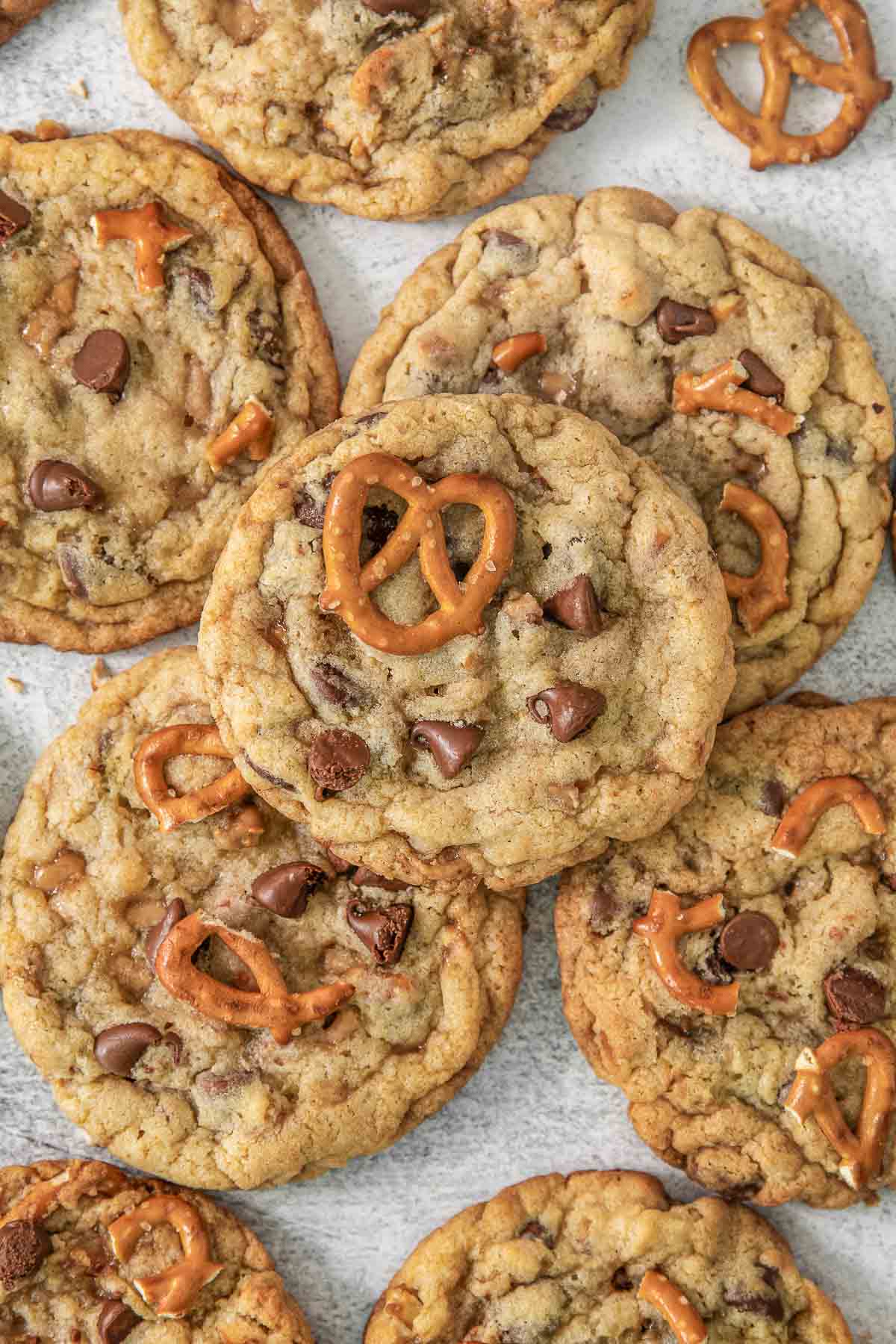 Multiple Kitchen Sink Cookies on a grey background surrounded by pretzels.