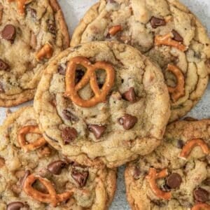 Multiple Kitchen Sink Cookies on a grey background surrounded by pretzels.