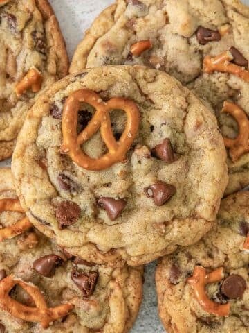 Multiple Kitchen Sink Cookies on a grey background surrounded by pretzels.