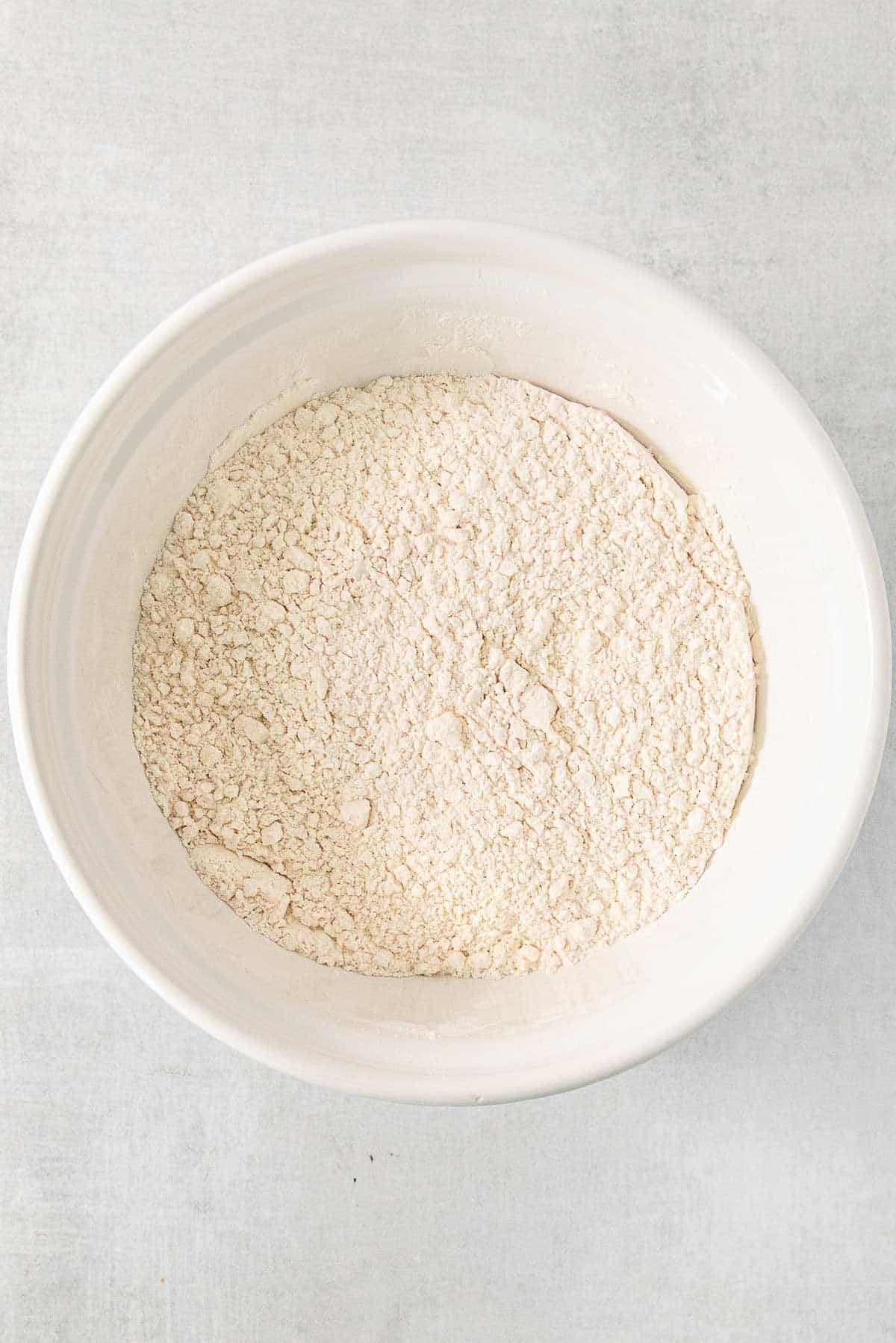 Flour in a white bowl on a white surface.