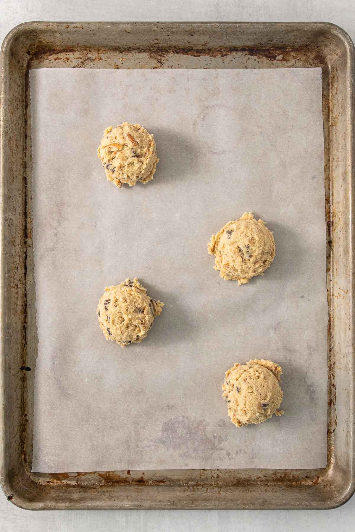 Four cookie dough balls on a baking sheet.