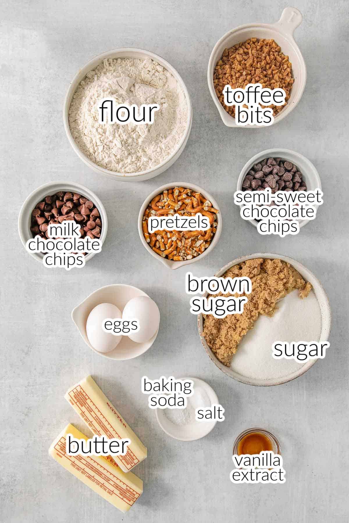 Ingredients for Kitchen Sink Cookies - flour, toffee bits, semi sweet chocolate chips, pretzels, milk chocolate chips, eggs, brown sugar, sugar, butter, baking soda, salt, and vanilla extract.