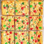 Multiple M&M cookie bars on a baking sheet with red and green sprinkles.