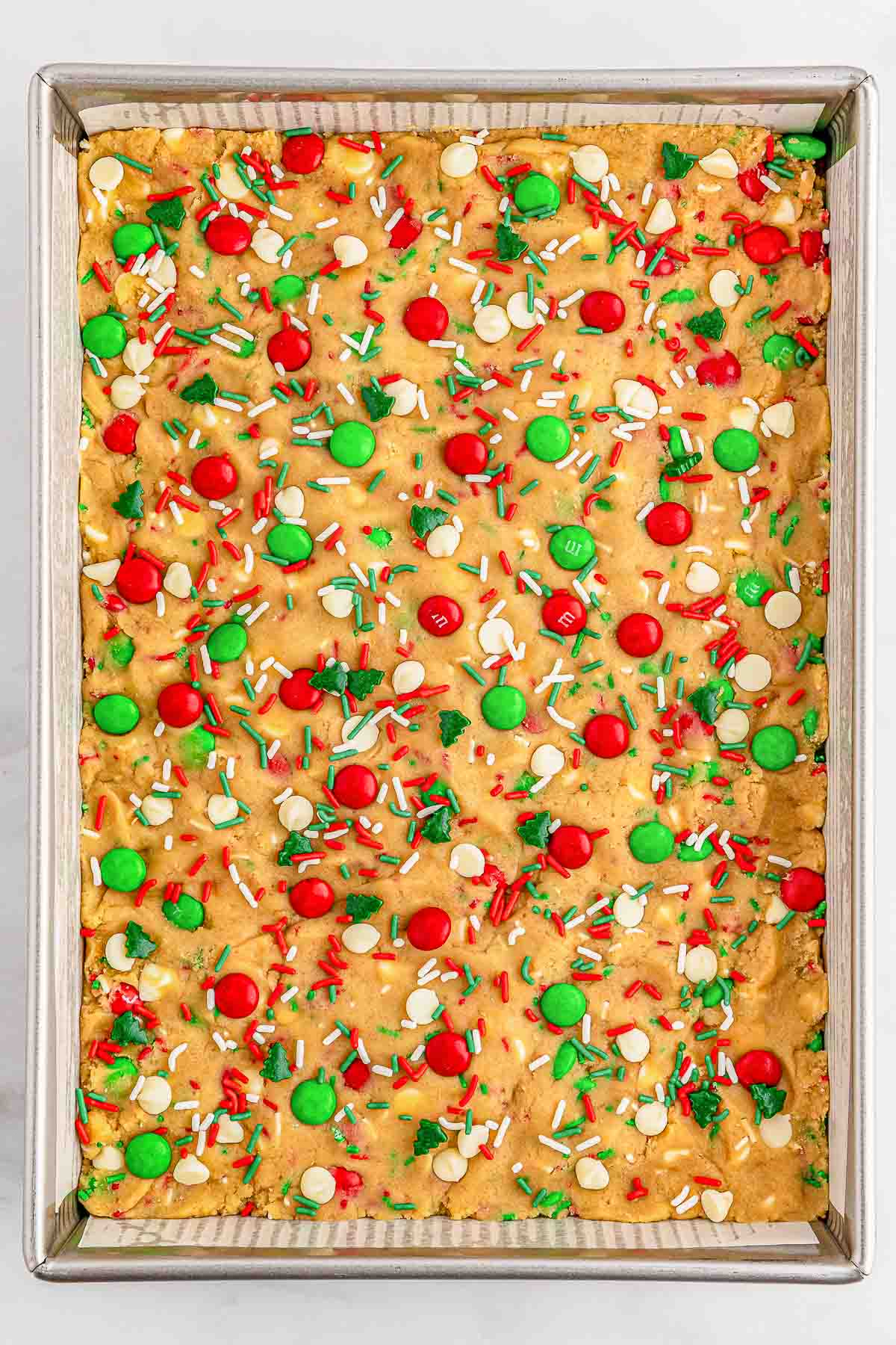 A baking tray with M&M cookie dough topped with red and green sprinkles.