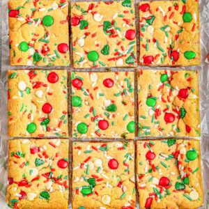 Multiple M&M cookie bars on a baking sheet with red and green sprinkles.