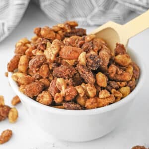 candied mixed nuts in a white bowl with a wooden spoon.