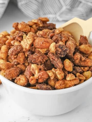 candied mixed nuts in a white bowl with a wooden spoon.
