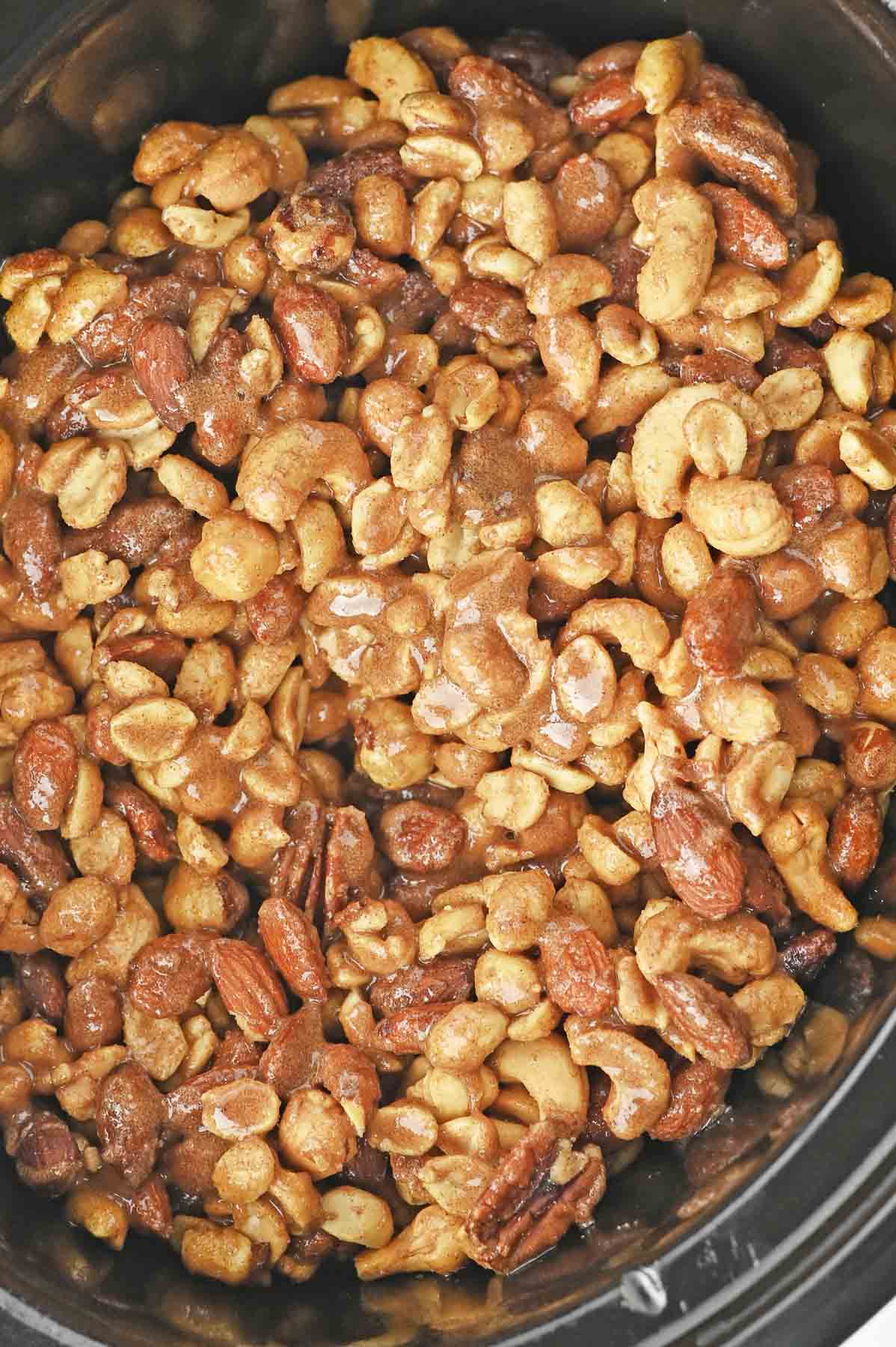 A crock pot full of nuts and pecans in a cinnamon sugar mixture.