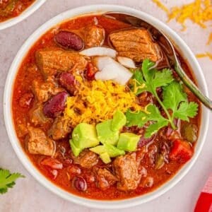 A white bowl of stew meat chili with cheese and guacamole.