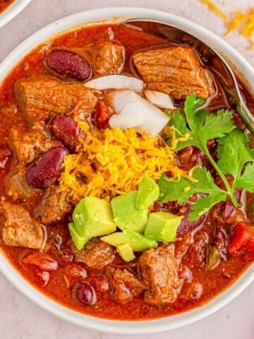A white bowl of stew meat chili with cheese and guacamole.