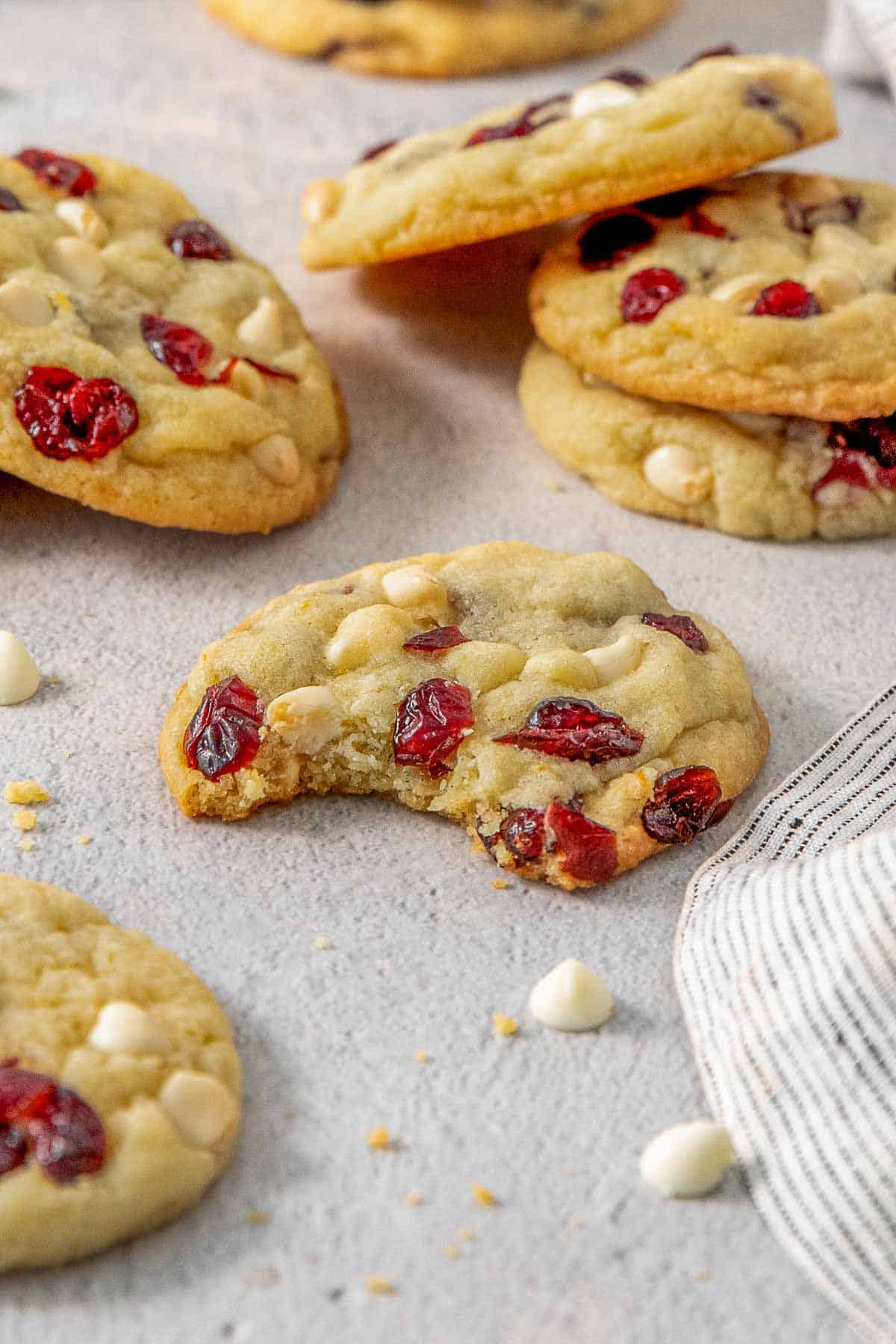 A white chocolate cranberry cookie with a bite taken out surrounded by several other cookies.