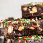 a stack of easy chocolate fudge with nuts and sprinkles on a white plate.