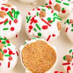 Several gingerbread truffles with vanilla coating and topped with red and green sprinkles and one cut in half showing the inside on a white plate.