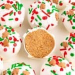 Several gingerbread truffles with vanilla coating and topped with red and green sprinkles and one cut in half showing the inside on a white plate.