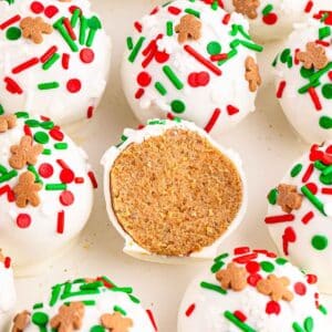 Several gingerbread truffles with vanilla coating and topped with red and green sprinkles and one cut in half showing the inside on a white plate.