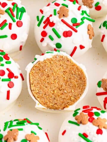 Several gingerbread truffles with vanilla coating and topped with red and green sprinkles and one cut in half showing the inside on a white plate.