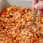 A person taking a spoonful of sweet potato casserole with streusel topping from a white casserole dish.