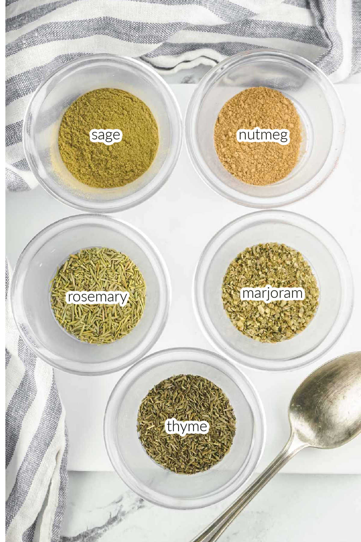 Five different types of herbs and spices for homemade poultry seasoning in small glass bowls.