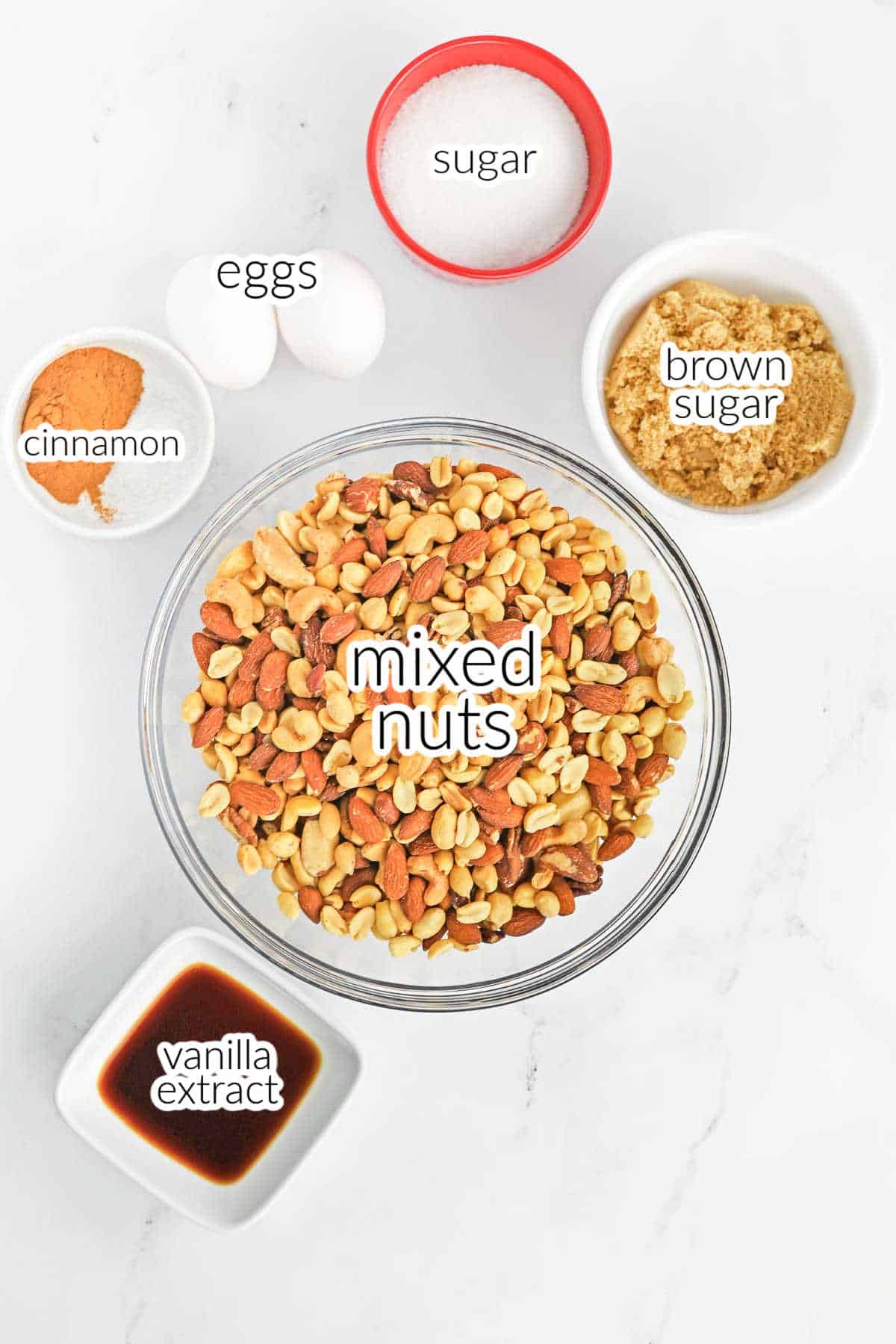A bowl of mixed nuts and small bowls of sugar, brown sugar, cinnamon and vanilla extract and 2 eggs for a candied nuts recipe.