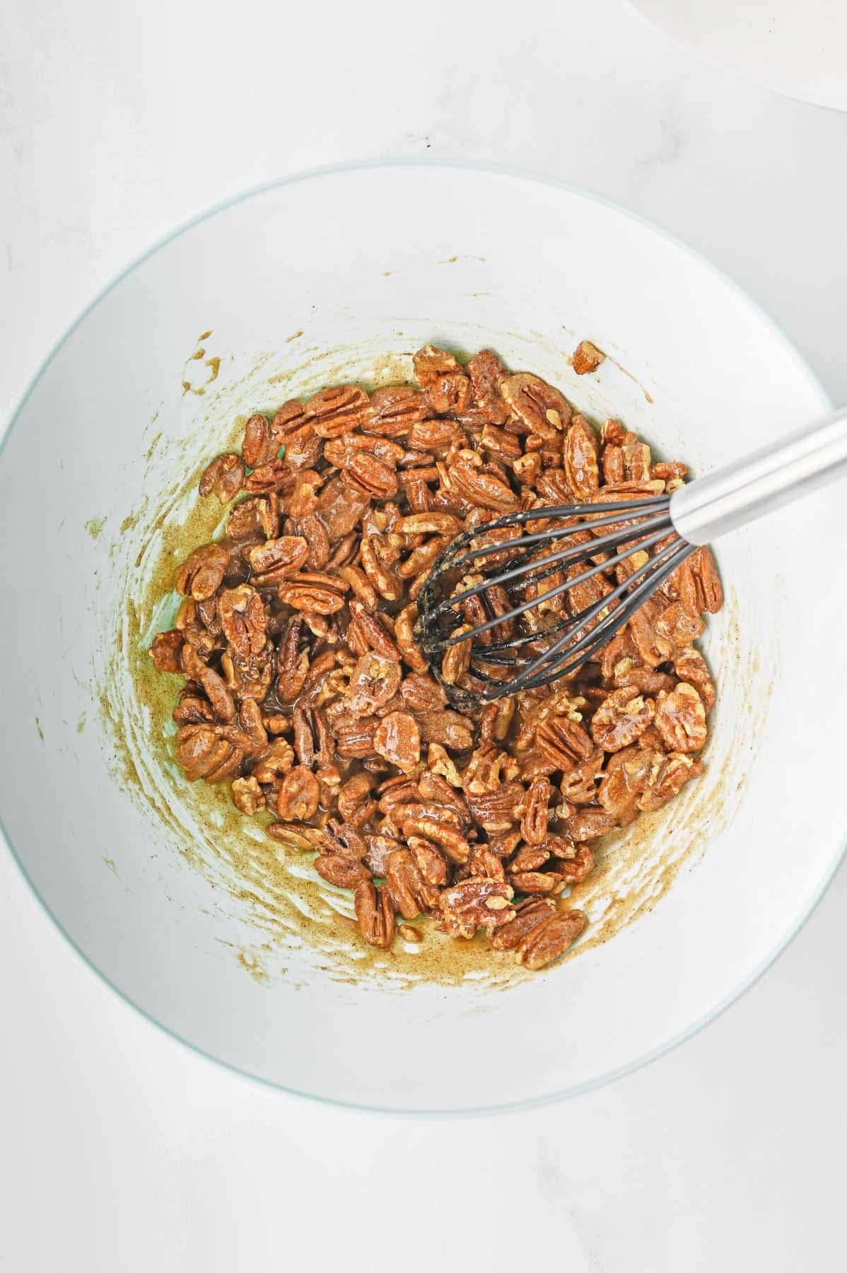 Pecans in a sugar mixture in a bowl with a whisk.