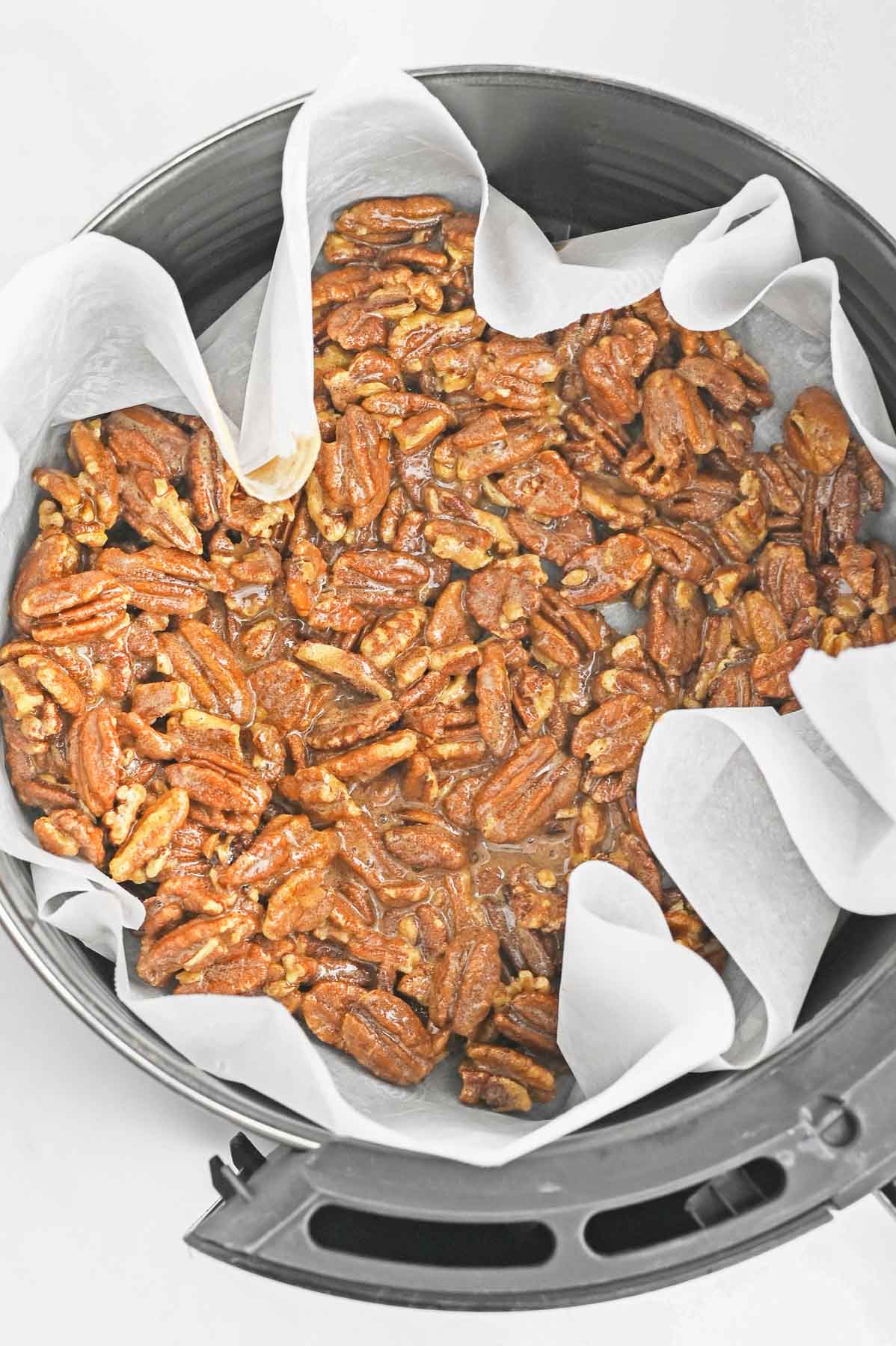 Pecans in an air fryer on a sheet of parchment paper.