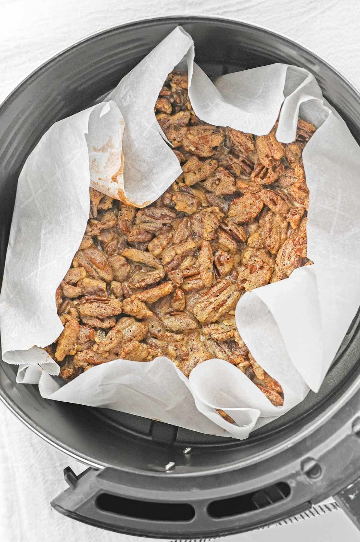 An air fryer basket filled with candied pecans.