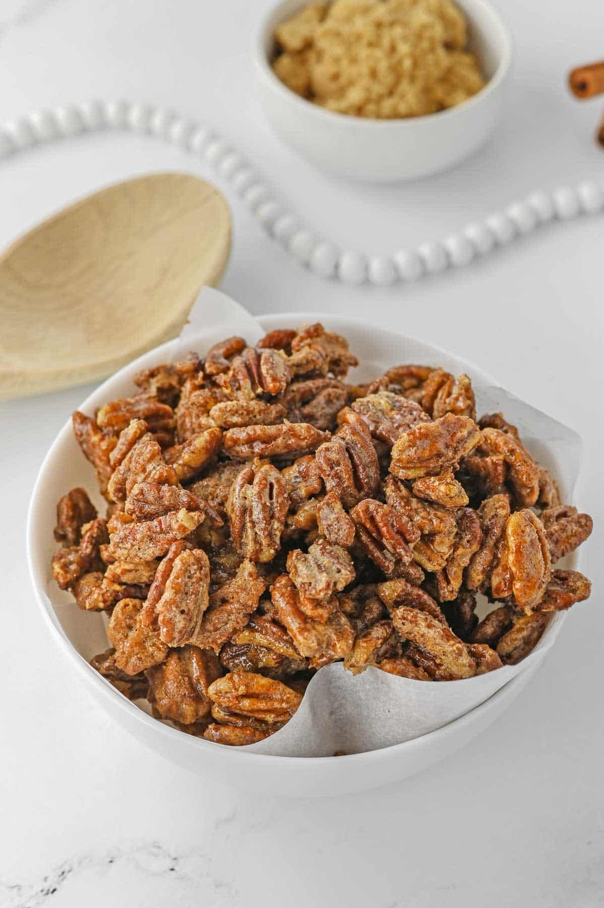 cinnamon sugar coated pecans in a white bowl on a marble countertop.
