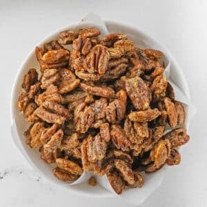 closeup of candied Pecans in a white bowl on a marble table.