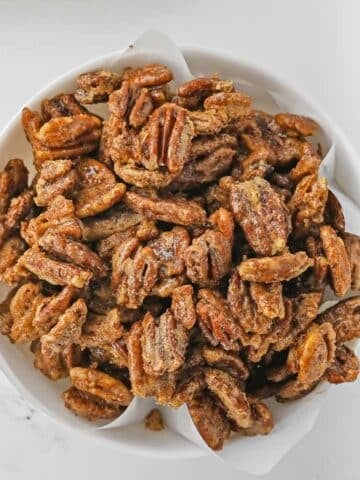 closeup of candied Pecans in a white bowl on a marble table.